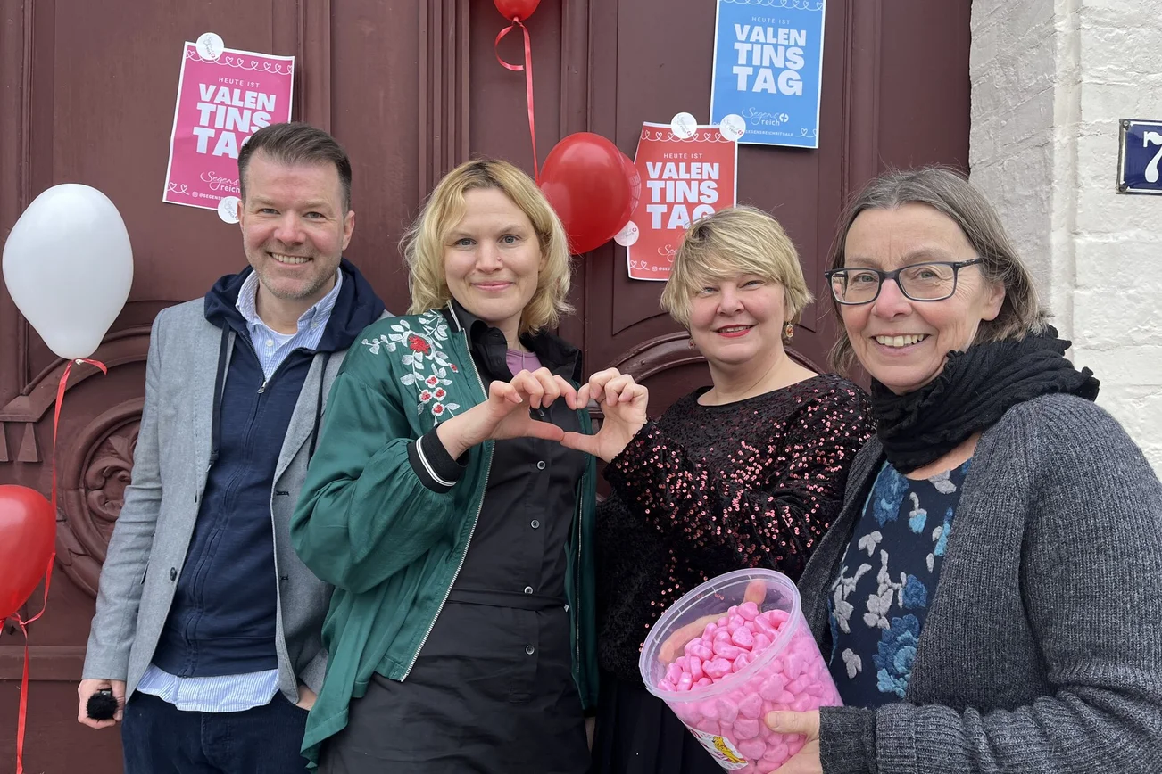 Ein Mann und drei Frauen stehen vor einer Kirchentür mit Plakaten zum Valentinstag.